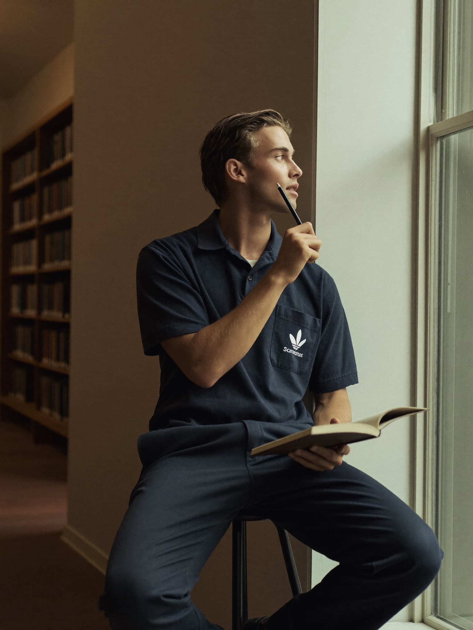 A learner practicing spoken answers aloud by a tall library window, notebook in hand