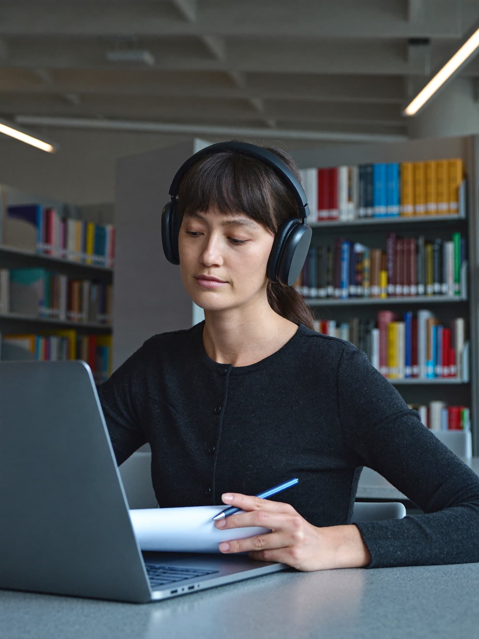 A student listening through headphones and writing answers in a quiet library
